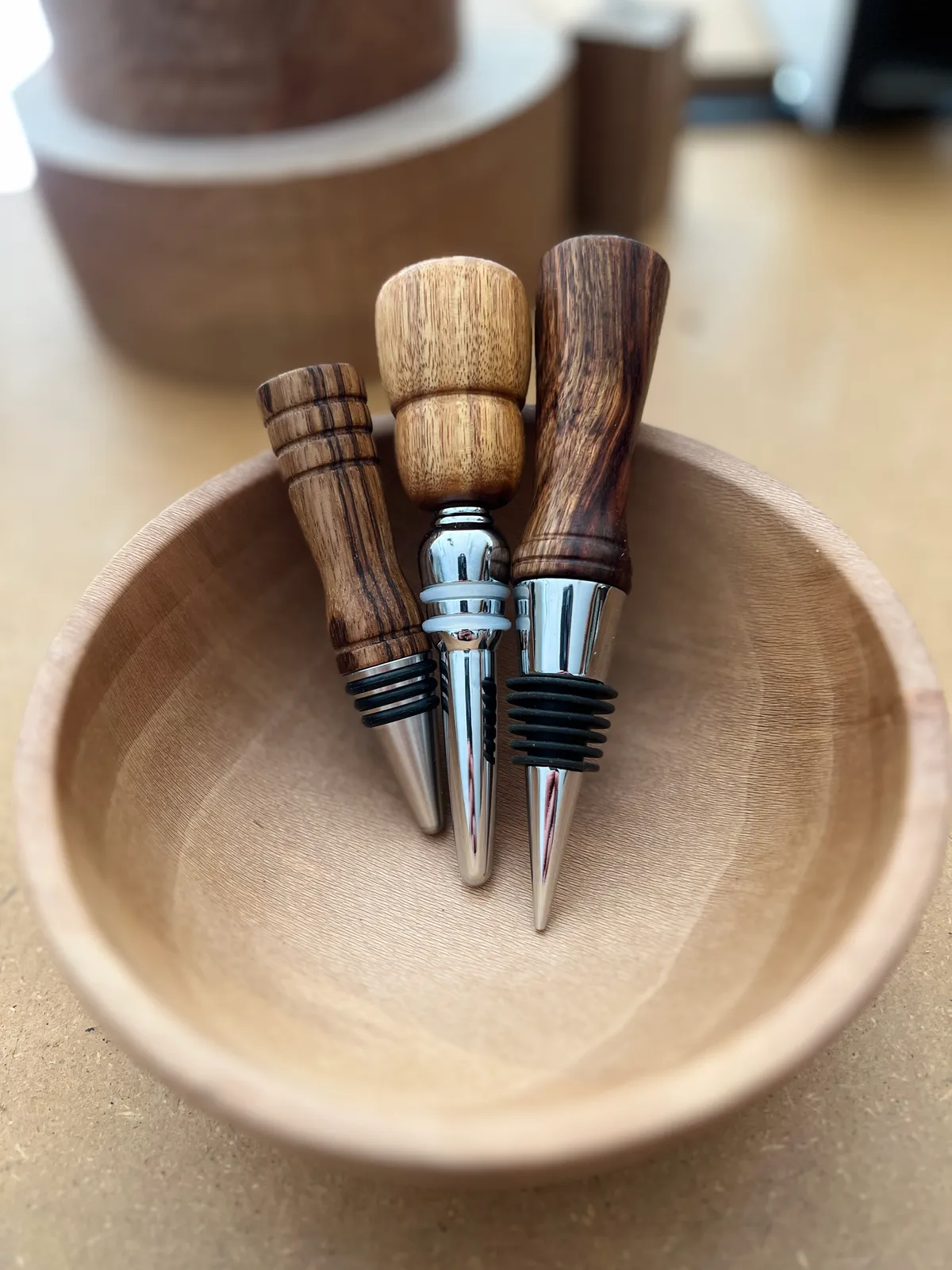 Three handcrafted wooden wine stoppers resting in a turned wooden bowl